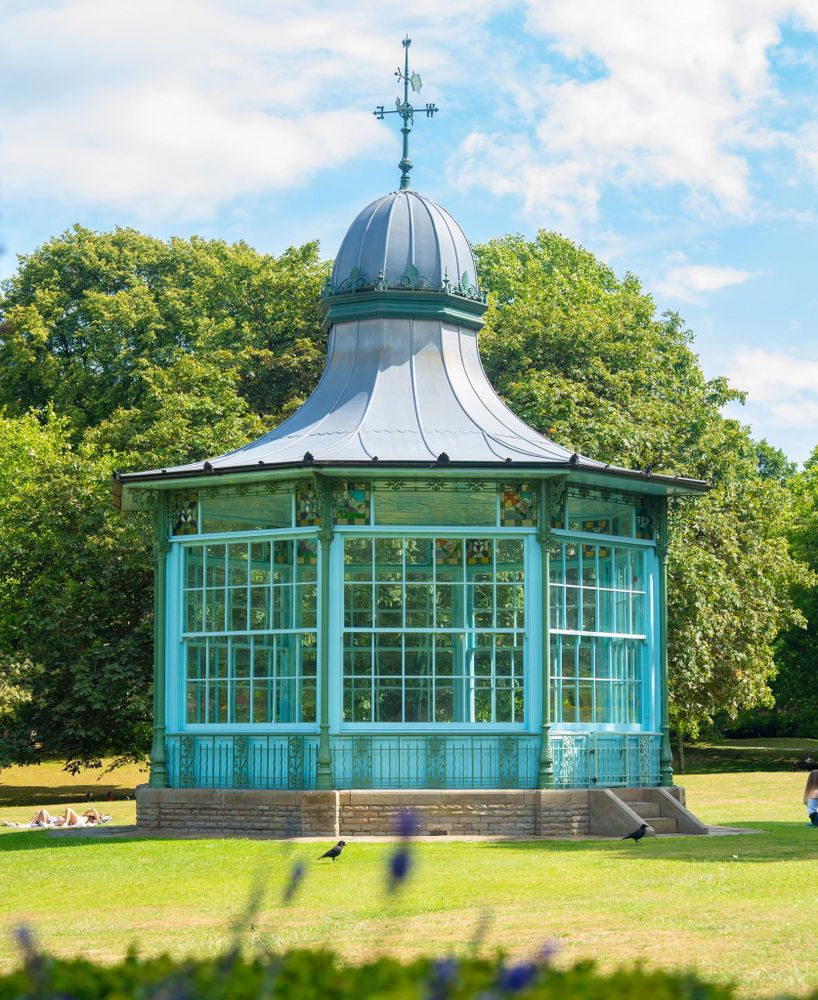 A blue band stand on a grass field in the sun, there are blue flowers in the foreground
