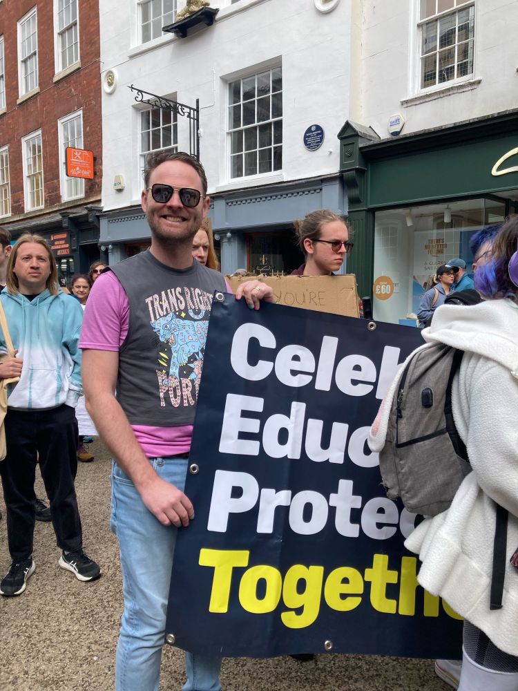 A man wearing a “trans right forever” crop top holding a banner which proclaims “Celebrate, Educate, Protect: Together” at a trans rights protest in Worcester city centre 