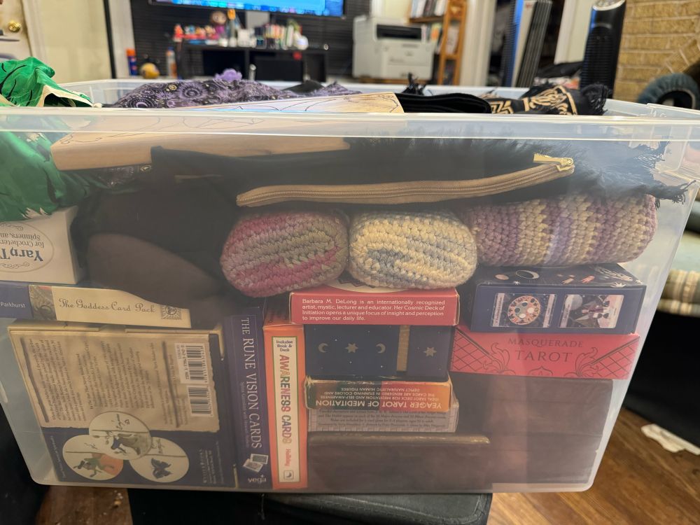 A transparent plastic tub containing an assortment of Tarot and oracle decks in their original boxes, in wooden boxes, in canvas zipper bags, and in hand-crocheted bags.