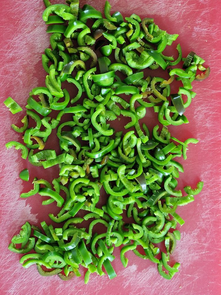 Pile of sliced jalapeños on red cutting board