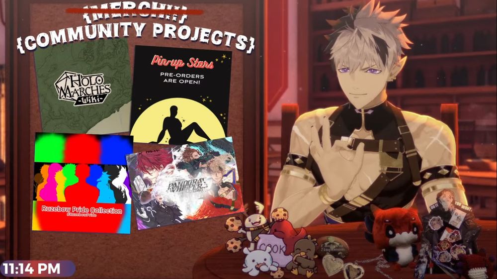 Screenshot of Crimzon Ruze's stream where there are images on a board with various community projects, such as Holomarches Wiki, Pin-Up Stars, Ruzebow Pride Collection and Pandora's Whisper. Ruze is sitting in front of a table with various drawings of little mascots, plushies, stickers and lockets.