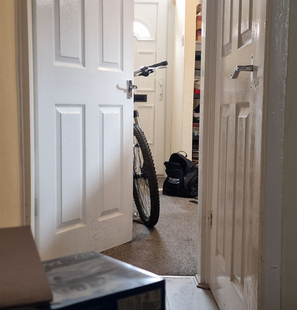 Front wheel and handlebars of a mountain bike seen through a doorway.