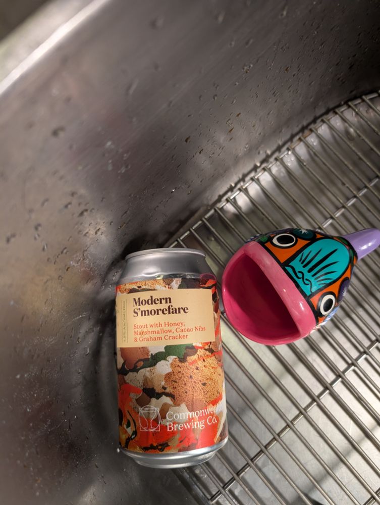 A can of Modern S'Morefare (Stout with Honey, Marshmallows, Cacao Nibs & Graham cracker) lays on the bottom of a sink with a Mexican sponge holder frog yelling at it 