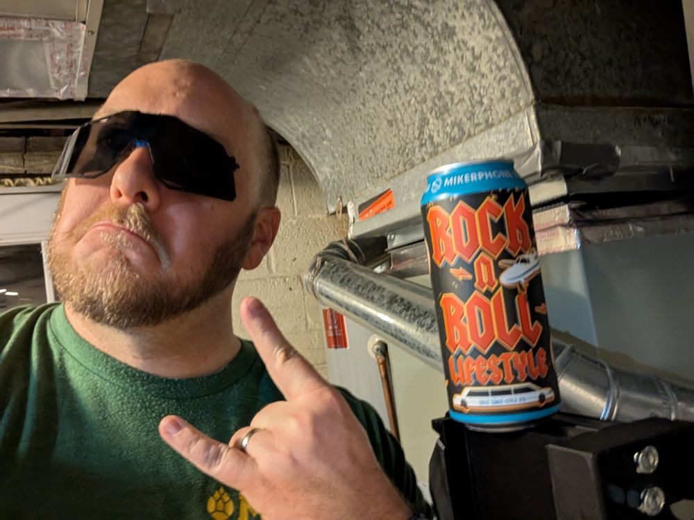 a very silly looking man throws the horns while balancing a cycling visor on his face, posing next to a can of Rock n Roll Lifestyle West Coast IPA