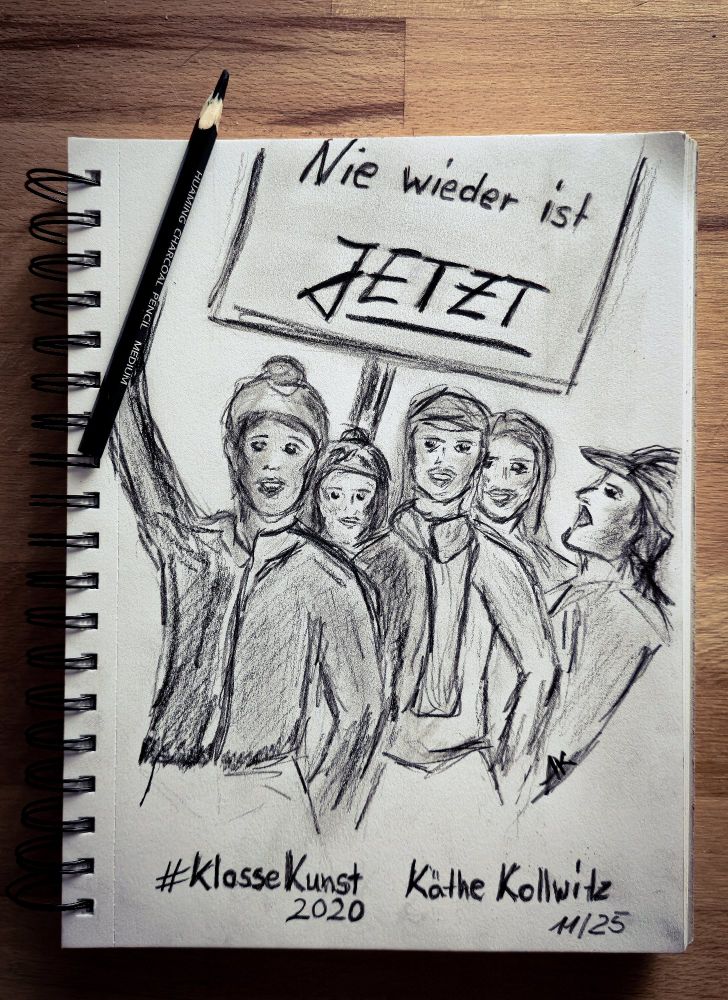 Eine Kohlezeichnung in einem Skizzenbuch zeigt eine Gruppe von Menschen, die demonstrieren. Eine Person hält ein Schild mit der Aufschrift „Nie wieder ist JETZT“. Auf dem Blatt liegt ein Kohlestift. Unten steht handschriftlich „#KlasseKunst 2020 Käthe Kollwitz 11/25“.