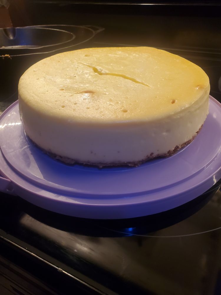Picture of a homemade cheesecake with a crack in the top.