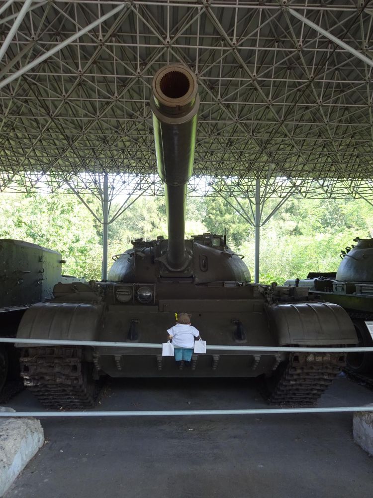 soft toy Lufsig in a white tee with two shopping bags facing a T-54/5 tank