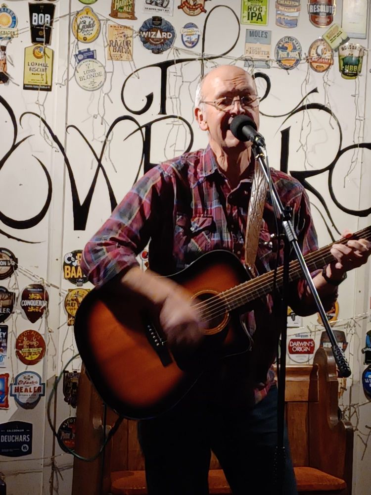Graham Armfield singing and playing guitar onstage.