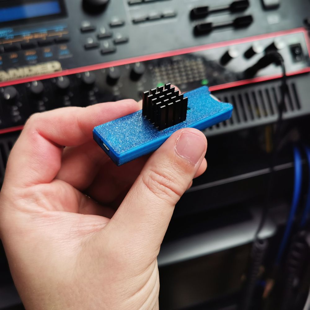 Holding a Teensy 4.1 computer chip, housed in a blue plastic sleeve, with a 15mm heatsink attached