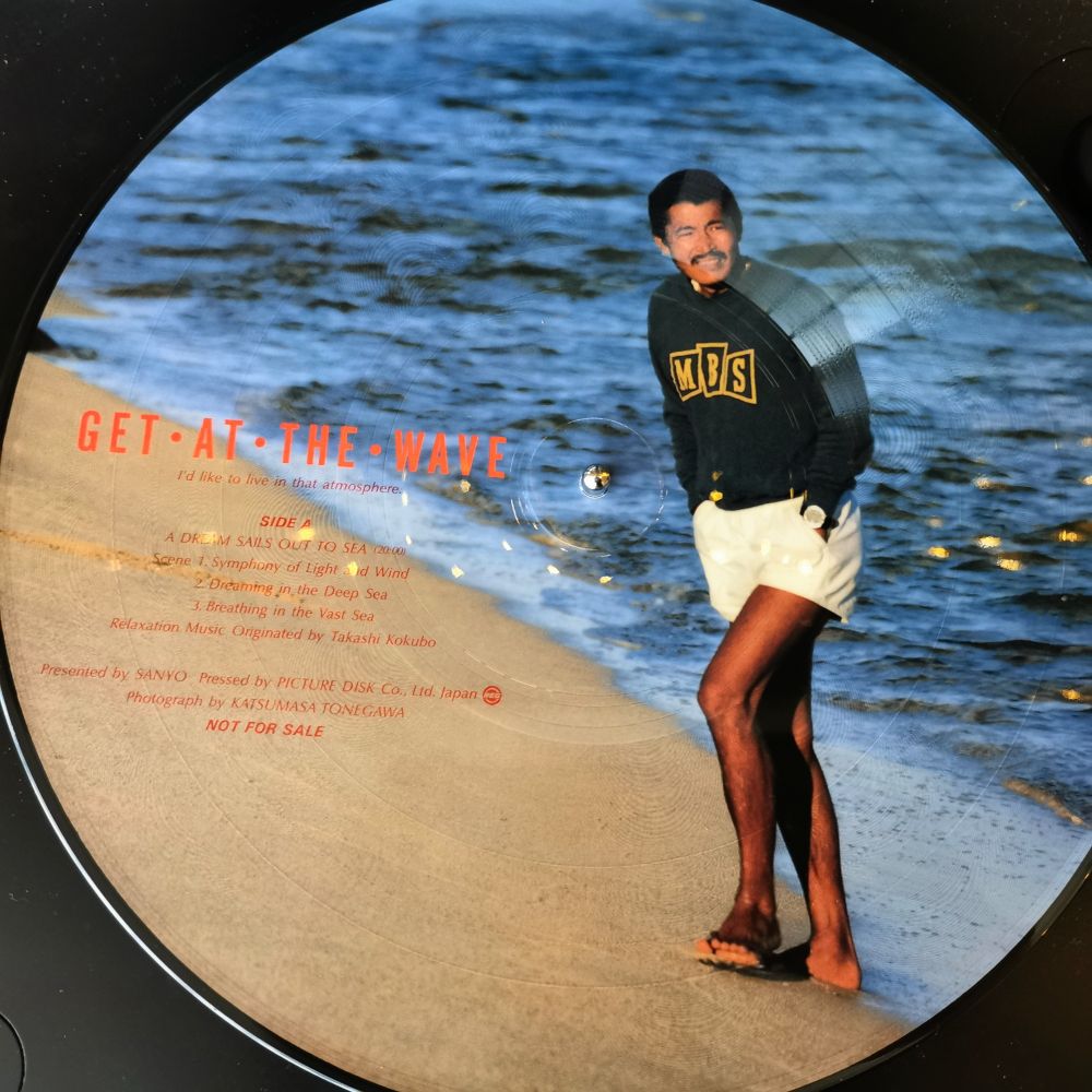 Vinyl picture disc featuring a man in shorts (Takashi Kokubo) standing on a beach 