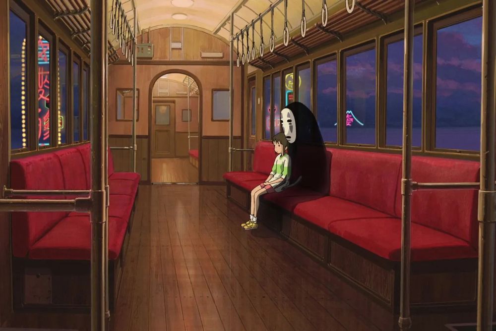 A still from Miyazaki's "Spirited Away", with a girl sat quietly in a train carriage with the supernatural creature "No-Face" and with night falling outside.