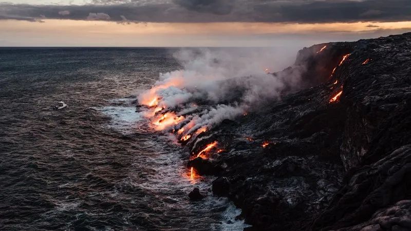 A fiery coastline where erupting lava is meeting the sea surrounded by plumes of steam.