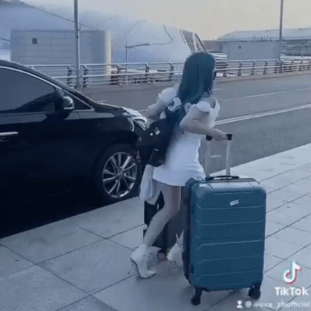 a woman in a white dress is pushing a blue suitcase on wheels