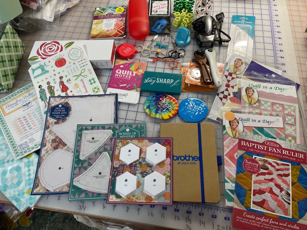 Sewing notions: stickers, templates, quilt in a day quilt patterns, Pettit scissors , color cards, jelly roll sasher, magnetic needle case, small quilt notes, small Brother journal, baby lock magnetic buttons, empty spray bottle, small rotary cutter with 3 blades, bobbin holders dark green & light green, tiny iron, pattern holder, small retractable tape measure, empty 3”x 9” box, 2.5”x 7” red tube case holders rotary cutter or other sewing notions. 