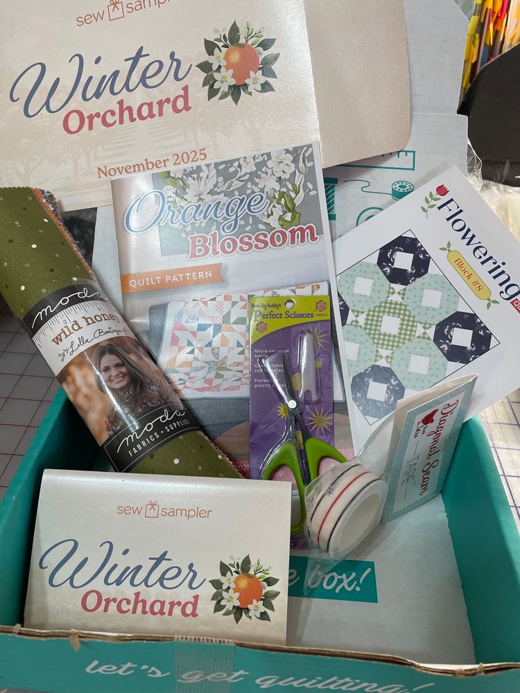 Received November 2025 Winter Orchard Sew sampler box: included is Wild honey jr layer cake fabric in autumn colors; diagonal seam tape 3 1/4” line markings; orange blossom mixed with squares and half square triangles; 4” lime green small scissors and #8 flowering quilt along block in blue, green, white fabric blocks. White and green corner squares 