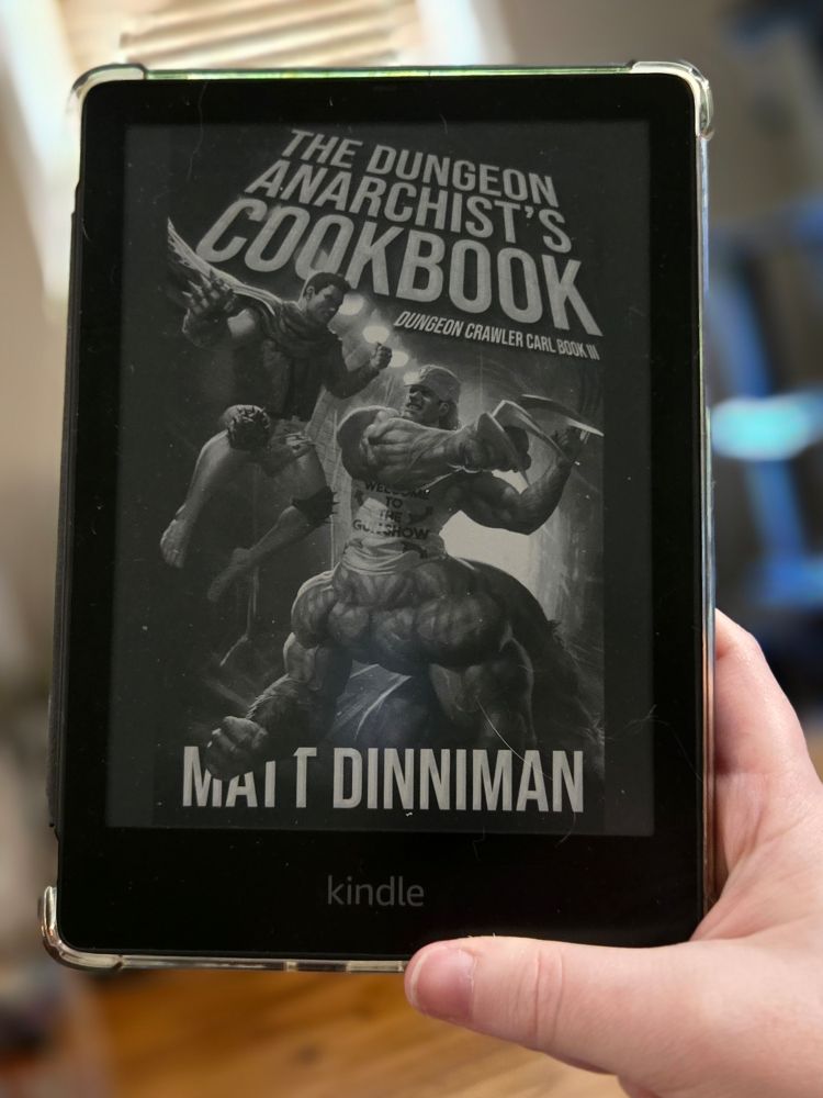 Black and white Book cover of The Dungeon Anarchist's Cookbook - Dungeon Crawler Carl Book III by Matt Dinniman on a kindle held by a small hand
