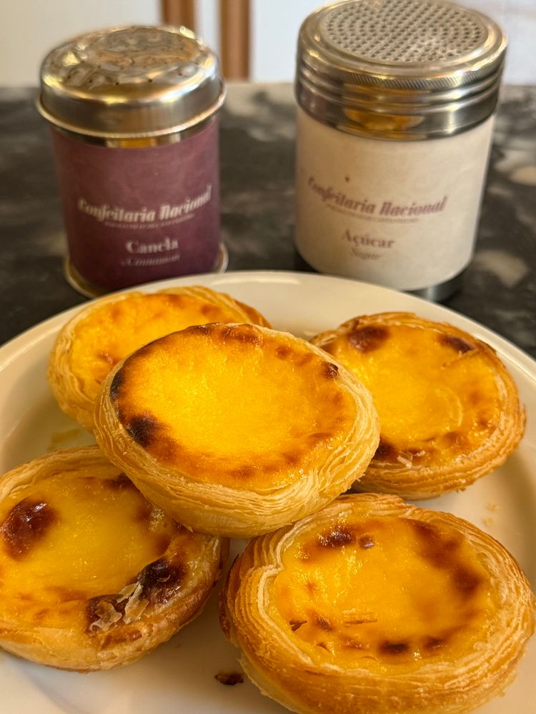 A plate of pasteis de nata with cinnamon and sugar shakers from Confeitaria Nacional in Lisbon 