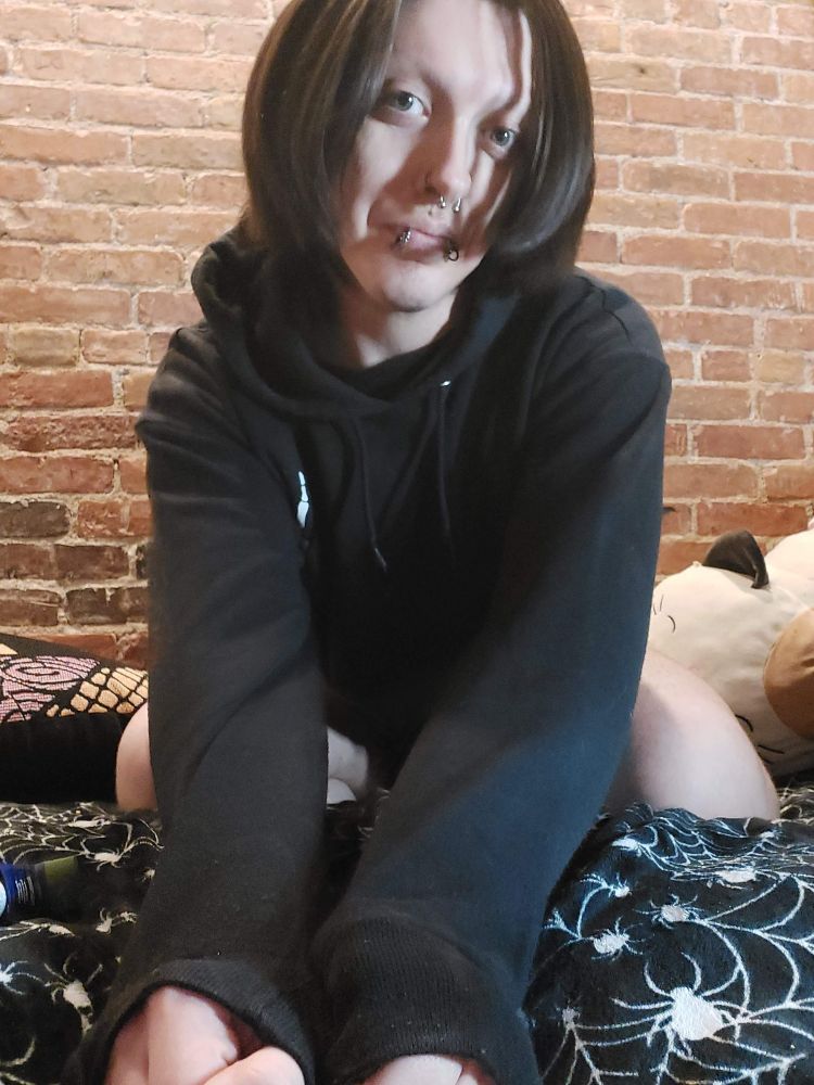 A boy is wearing long sleeves with his arms in front of him and has hair in his face, facing the camera. There is a brick building behind him.