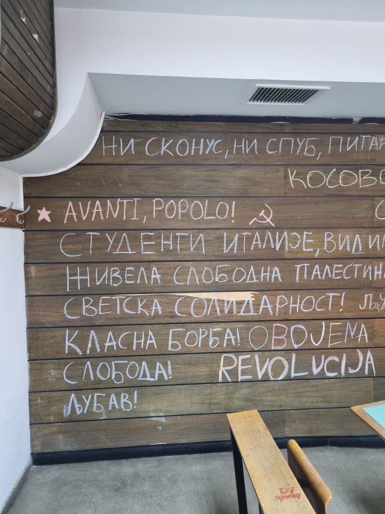 En vegg fullskrevet av setninger på serbisk, men den tredje linjen leser "avanti popolo!" etterfulgt av en enkel tegning av en hammer og en sigd. 