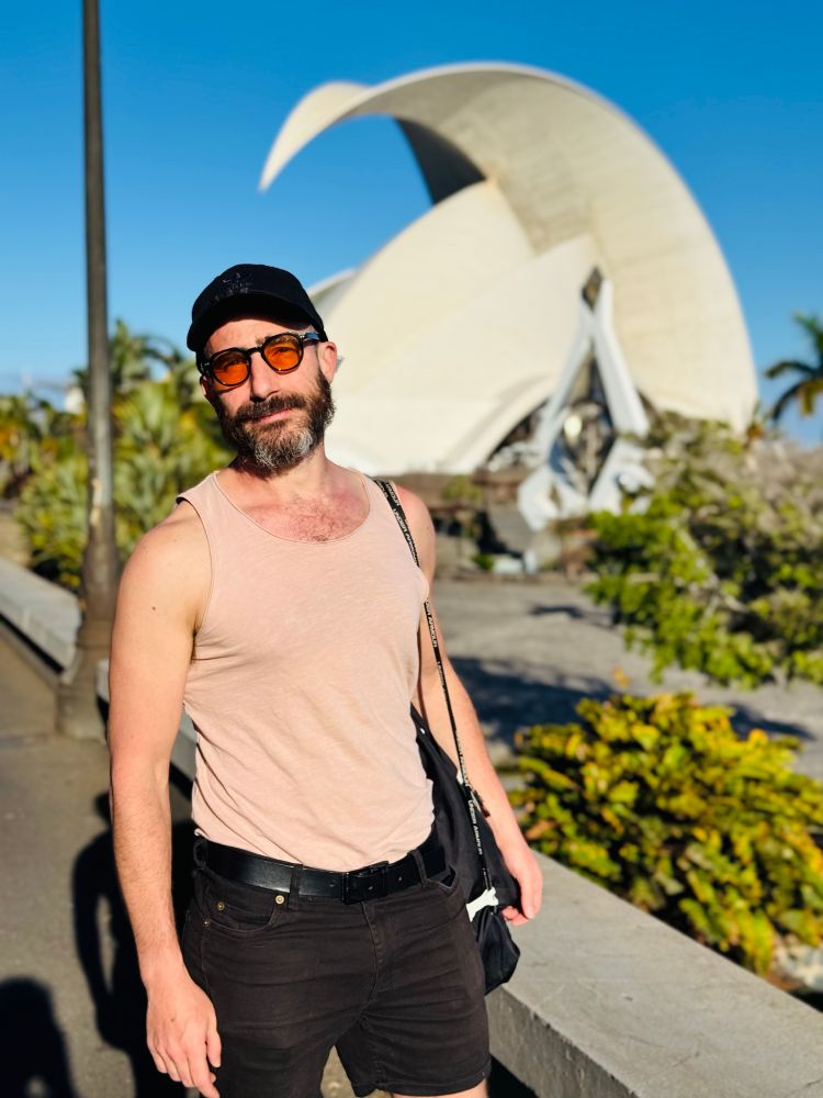 Photo of Julien in front of the Auditorio de Tenerife Adán Martín by Architect Santiago Calatrava. It's warm, he's in a tank top with sunglasses.