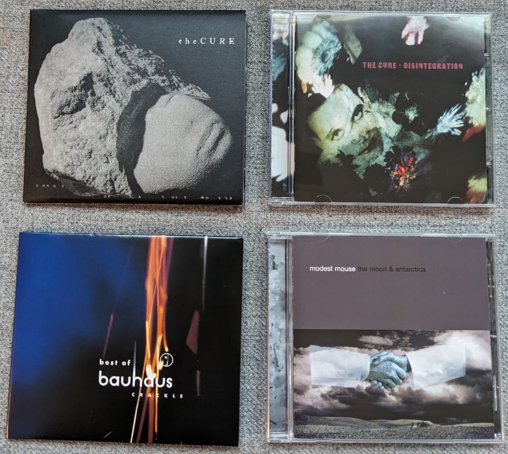 Four CDs. Top Left: Songs of a Lost World by The Cure. Top Right: Disintegration by The Cure. Bottom Left: Crackle The Best of Bauhaus. Bottom Right: The Moon and Antarctica by Modest Mouse. 