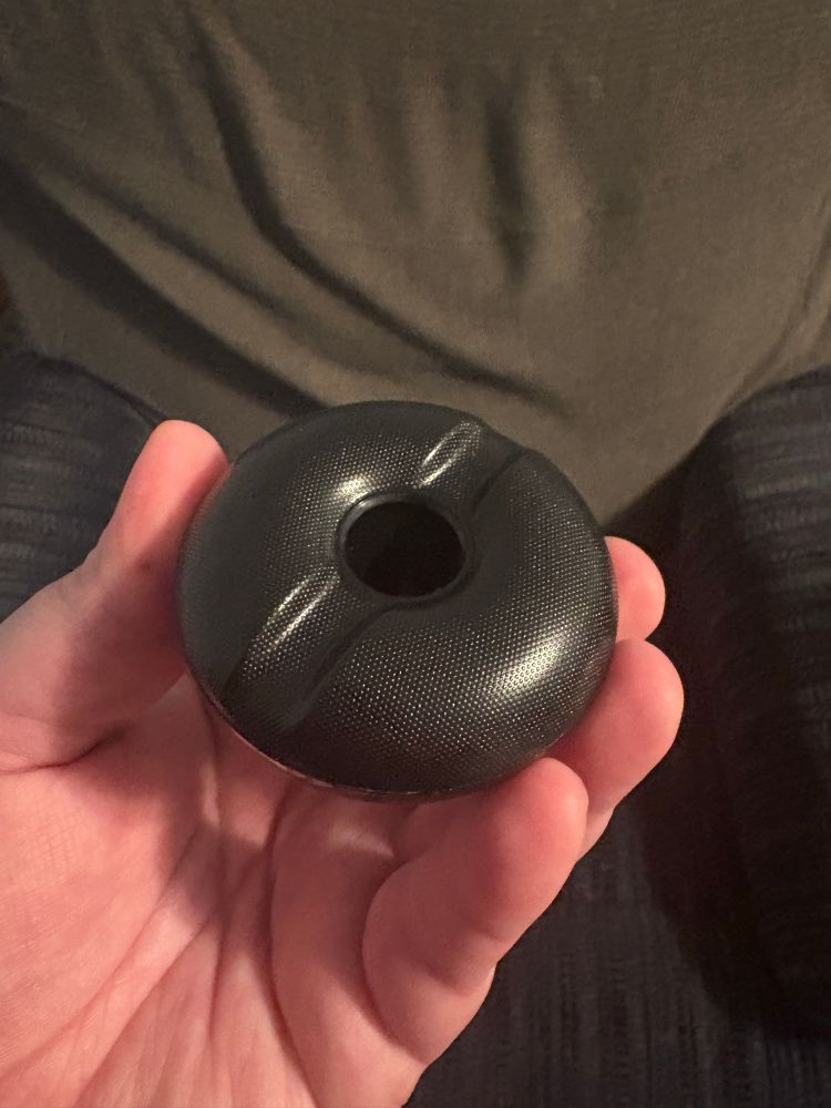 A black pen holder for a drawing tablet pen. The top is textured, with a groove cut along its diameter.