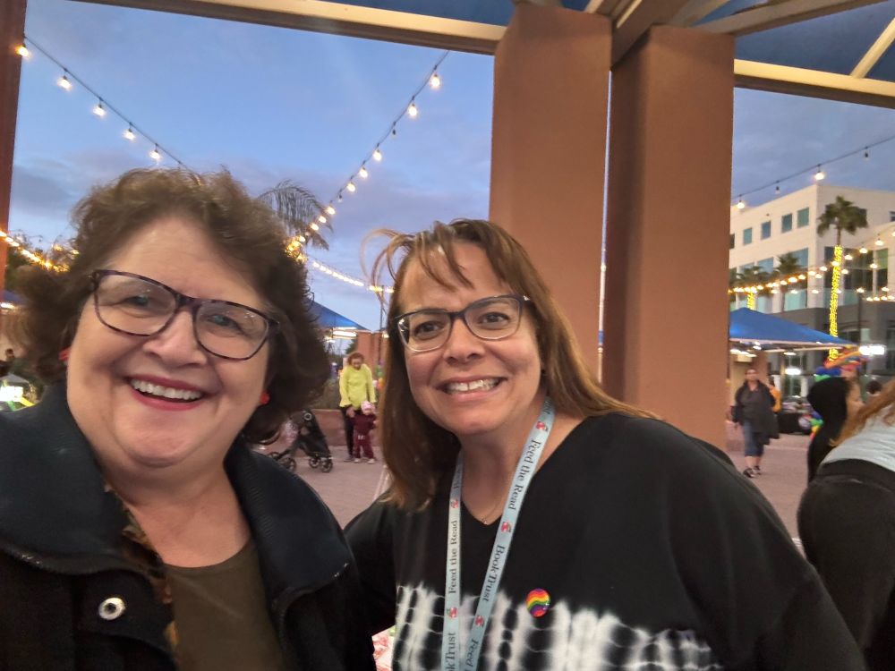 Mitzi Epstein and Zeyna Pruzhanovsky smiling with party lights overhead, and a street festival background