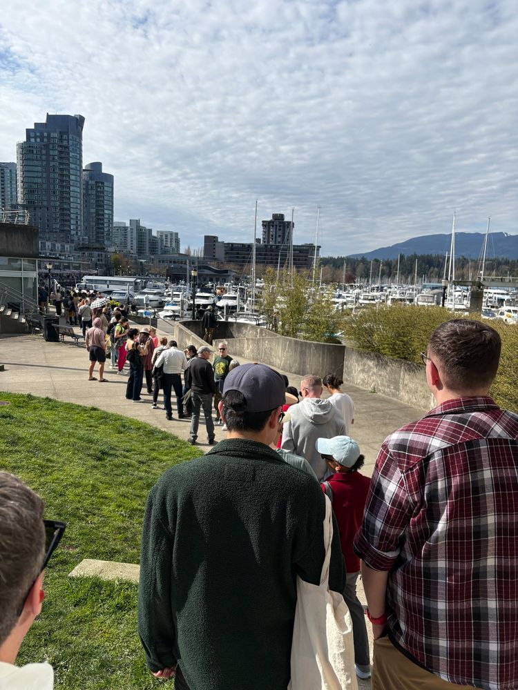 2 plus blocks of people lined up to vote along scenic Coal Harbour, water, boats, mountains in background