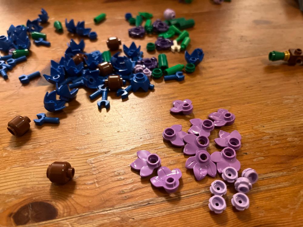 Parts of Lego flowers in shades of purple, blue and green scattered on a table.