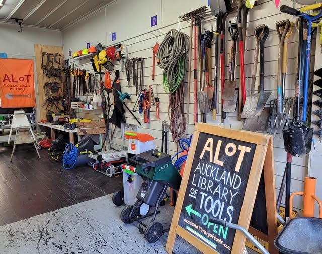 Photo of the inside of Auckland Library of Tools. A large sandwich board sign which says "Auckland Library of Tools, Open" is visible, as well as a wall lined with gardening tools, saws and clamps. 