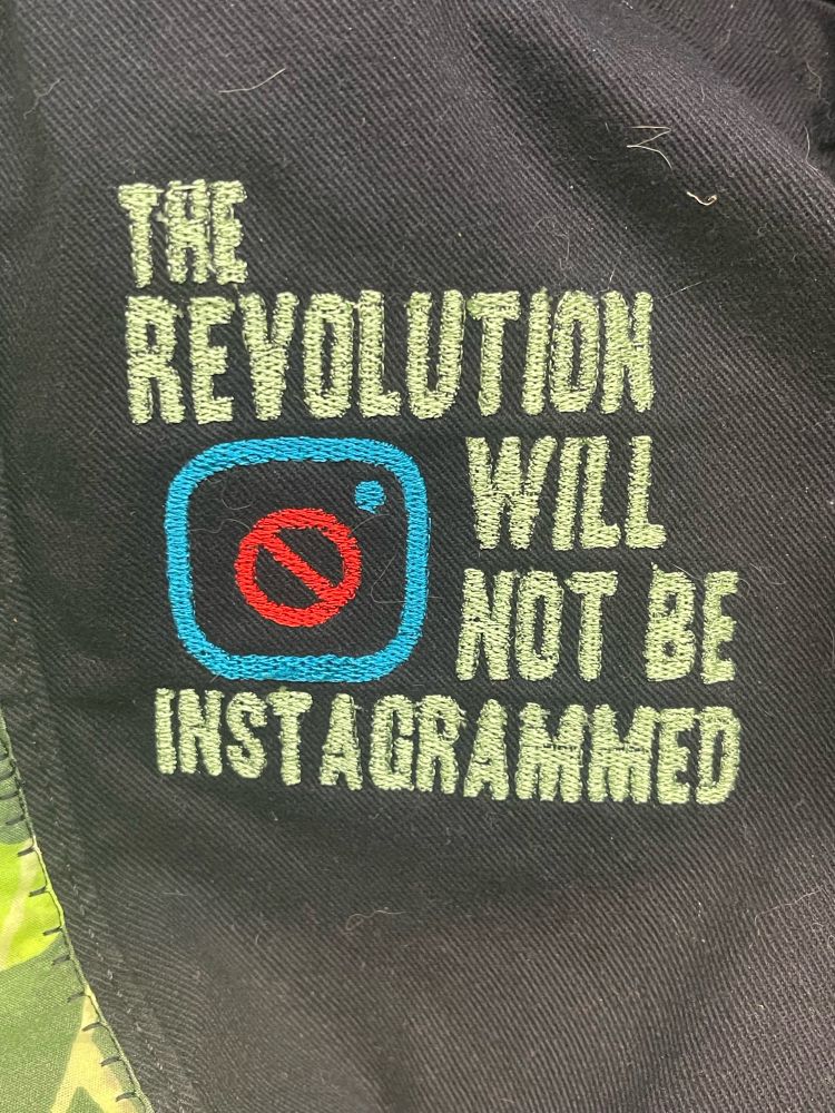 The Revolution Will Not Be Instagrammed embroidery on black denim vest. 