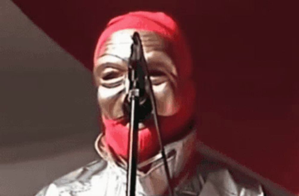 a person with a red mask on their face is singing into a microphone