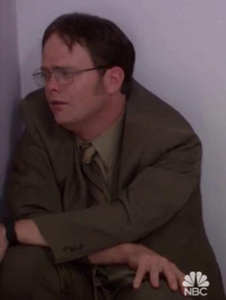 a man in a suit and tie is sitting in a corner with his hands on his knees .