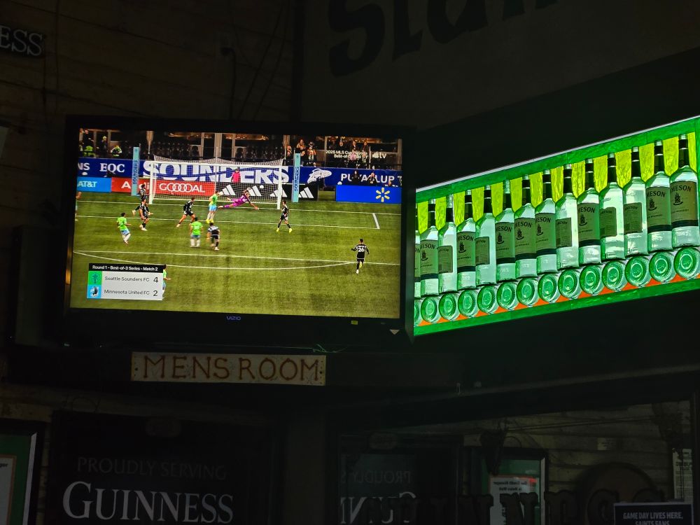 A TV with the Sounders match on next to a stained glass window made of Jameson bottles.