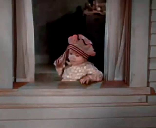 a baby is looking out of a window wearing a hat and holding a towel .