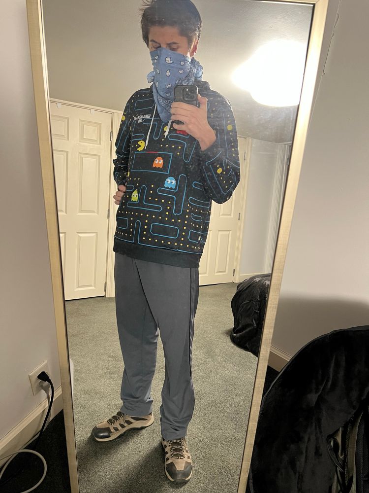 A mirror selfie of IRL me, partially face revealing with a bandana covering my lower face, who is looking downward with a slightly “resting angry” expression. I have my hand on my hip and attempt to make a sassy pose with my phone in my left hand taking the shot and a hip thrusted out.