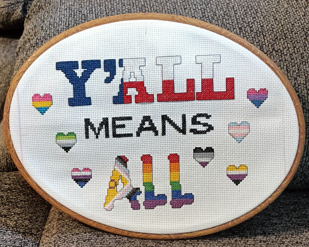 Cross stitch that says y'all means all with small pride hearts 