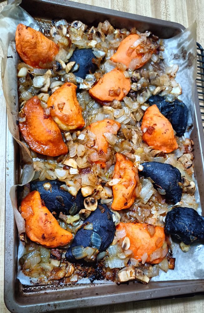 Orange and black perogies with onions and mushrooms on a cookie sheet