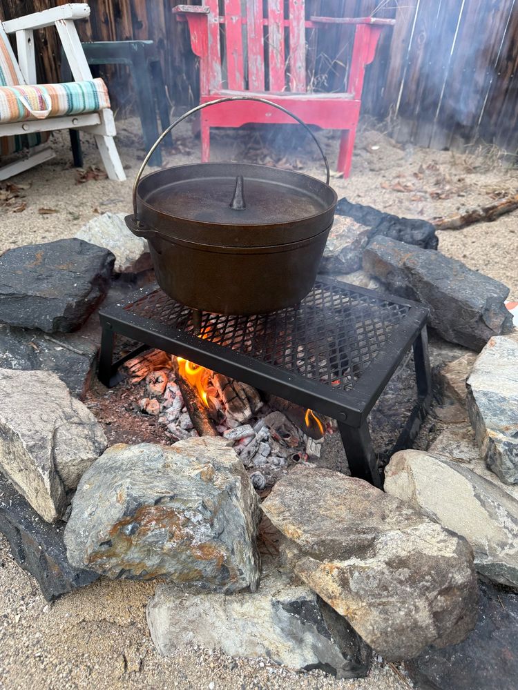 A Dutch oven sits on a metal grate over an open fire