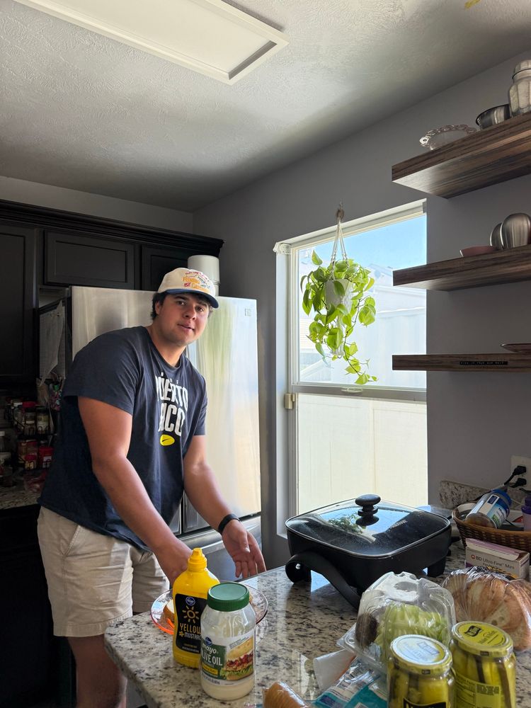 A young, muscular man in his 20s ,wearing a baseball cap, prepares to make a sandwich
