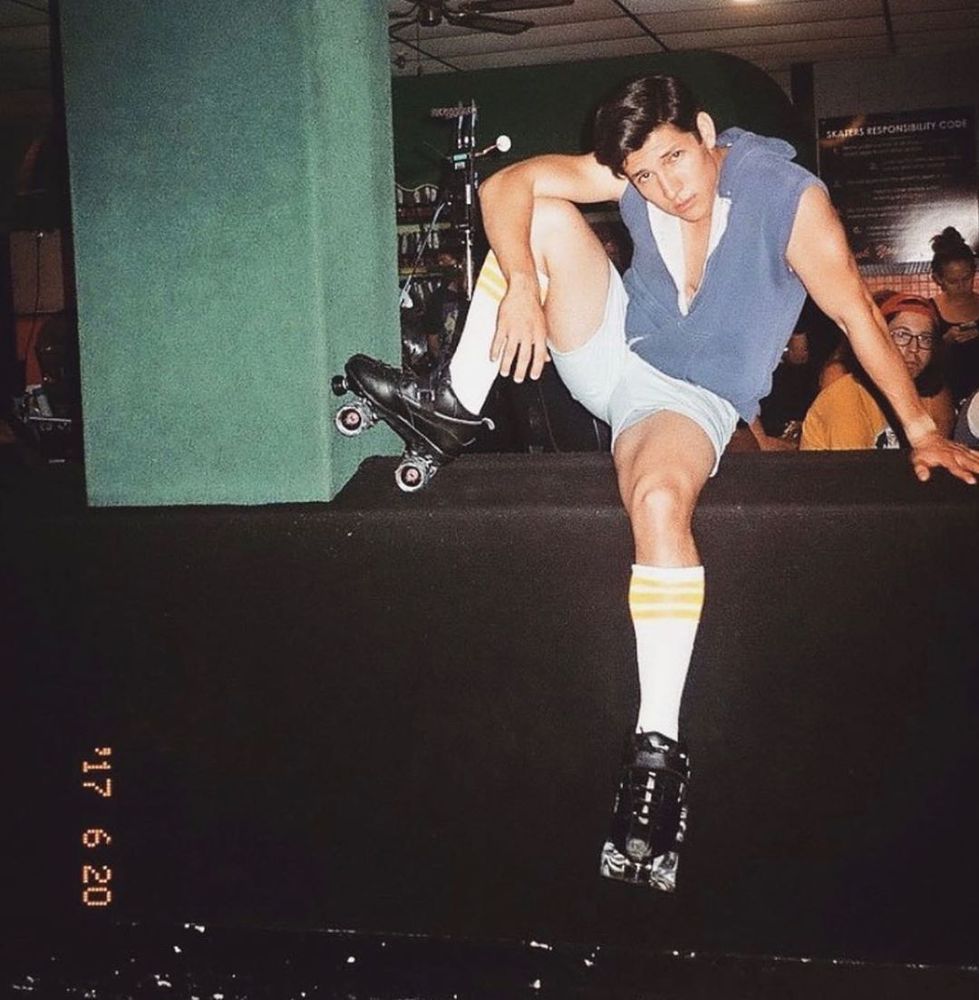 a fuzzy photo taken on film, the attached date reading 17 6 20, of a man wearing roller skates, shorts, knee socks, and a mostly unzipped hoodie vest perched on top of a wall. he has his right foot up and he's looking at the camera.