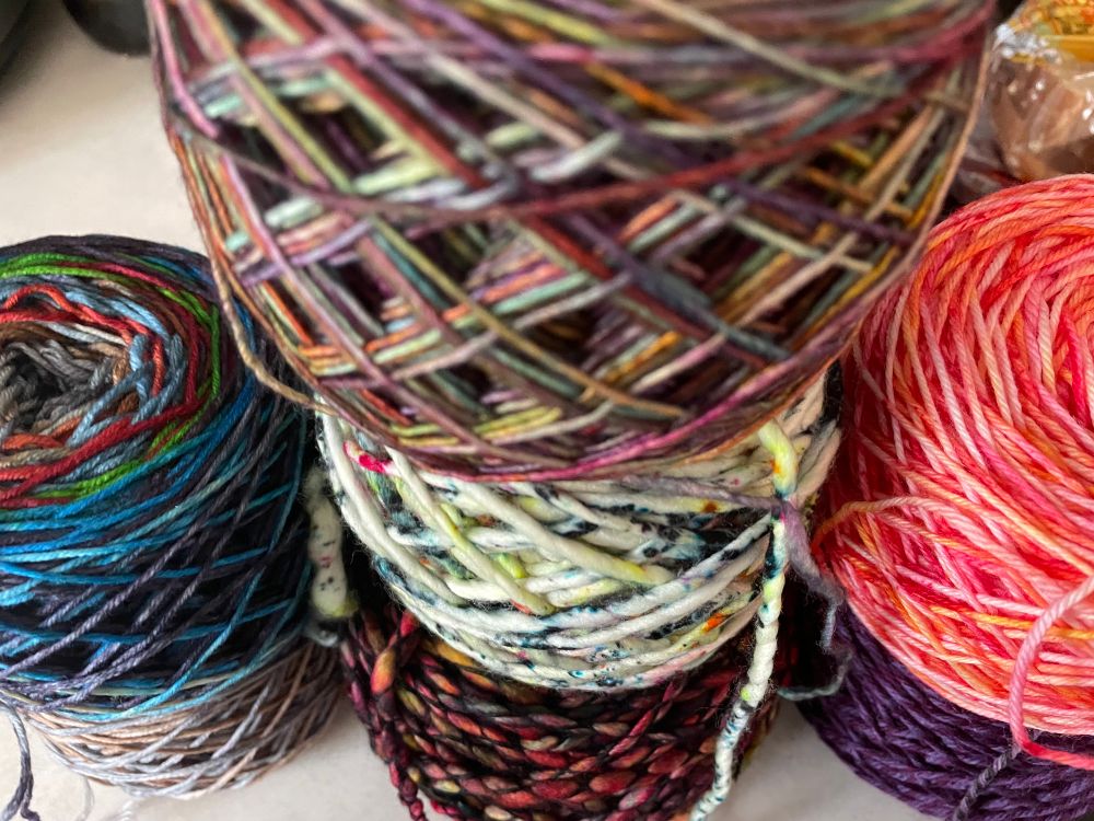 7 skeins of yarn. Grey, blue, red, purple, pink, white with speckles, and lavender. 