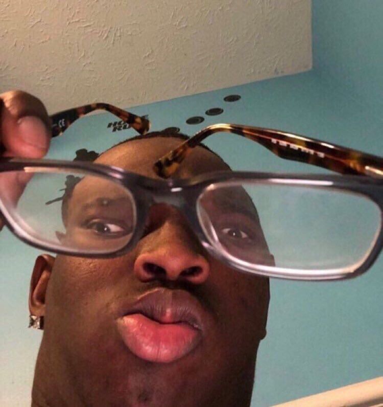A close-up of a man looking down directly into the camera with his right eye pointed in a completely different direction than his left eye. He's holding up a pair of reading glasses in a way that exaggerates the funny eye positioning.