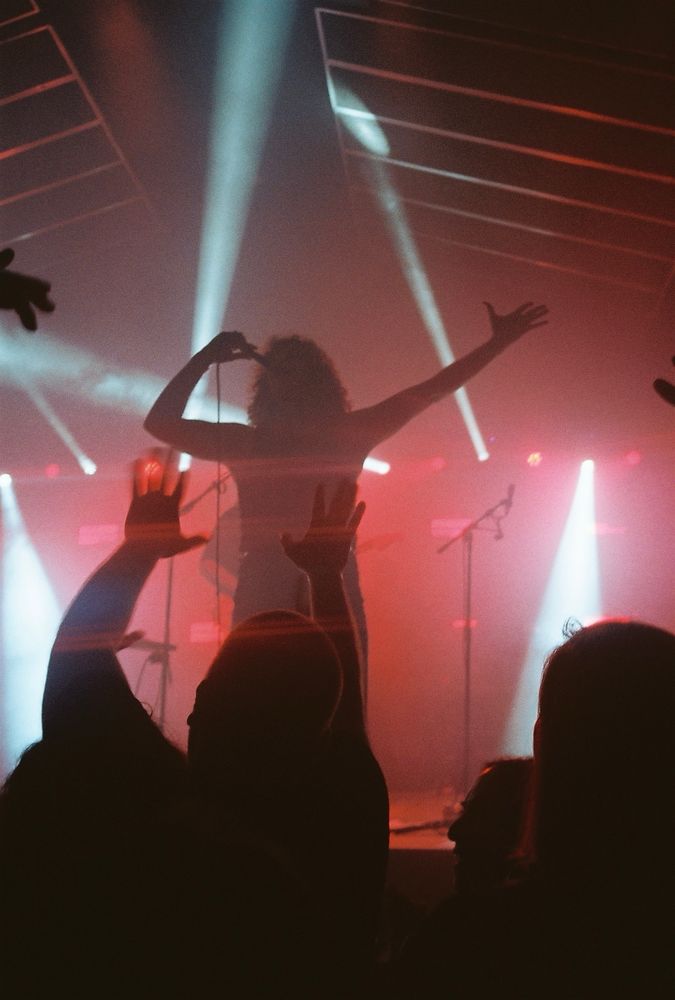 Photograph of a singer in front of a crowd backlit with blue and red lights. 