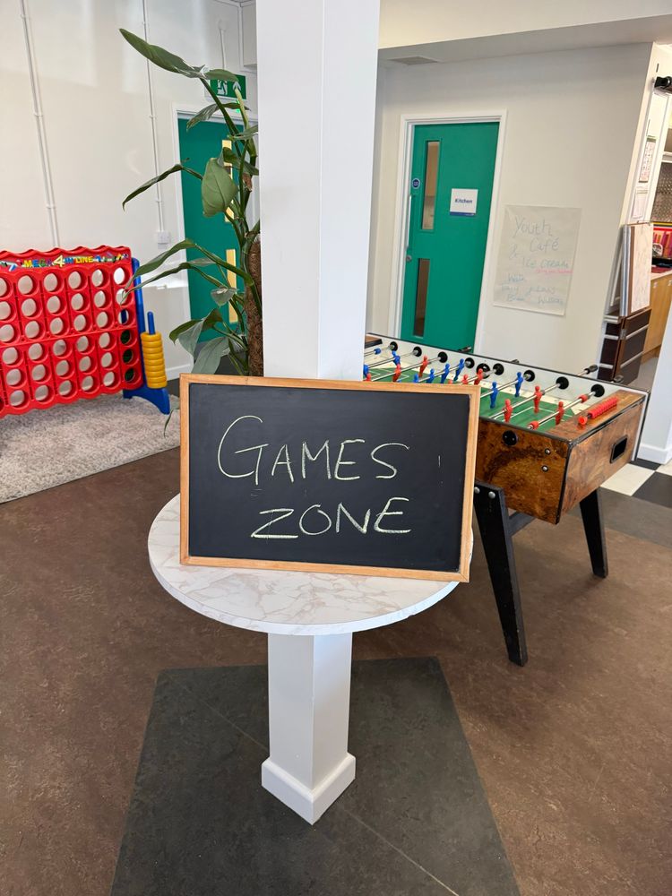 A sign in a table saying “games zone” with a football table and other games in the background 