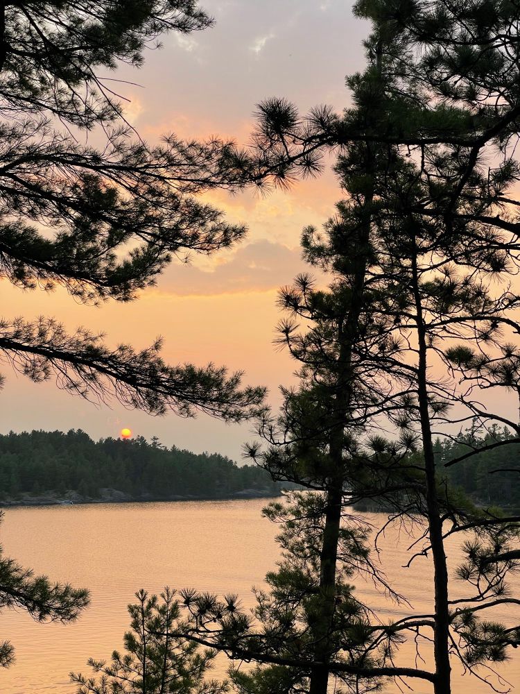 A sunset over 18 Mile Island on the French River in Ontario. Pink & orange sepia tones are muted by haze from distant wildfires. 