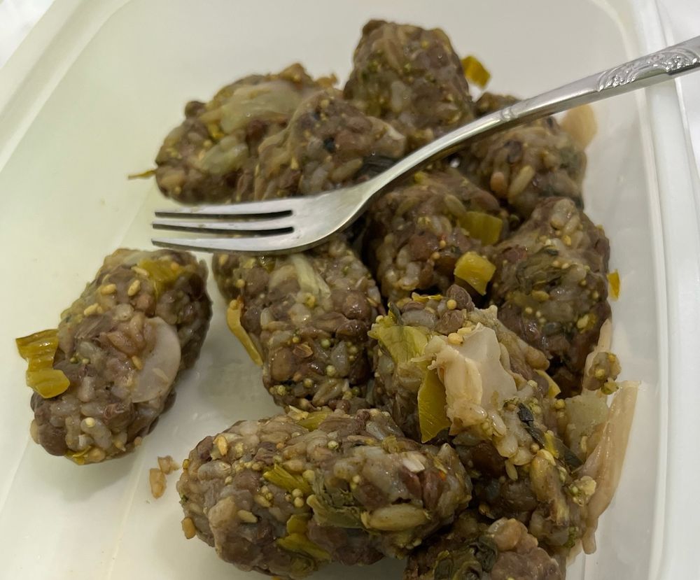 본죽통 안에 한입크기의 밥덩이들이 들어있다 절인 갓이 섞여 있고 색깔은 갈색이다