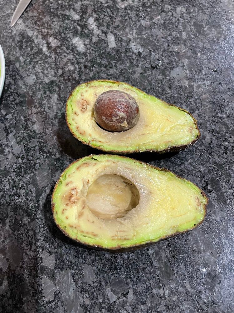 An avocado cut in half which is clearly overripe and Brown inside 