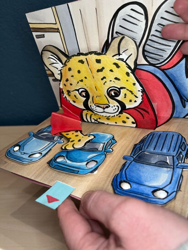 A pop up card with an anthropomorphized cheetah laying on the ground pushing toy cards into the correct order. When the cars move into place, their lights turn on.