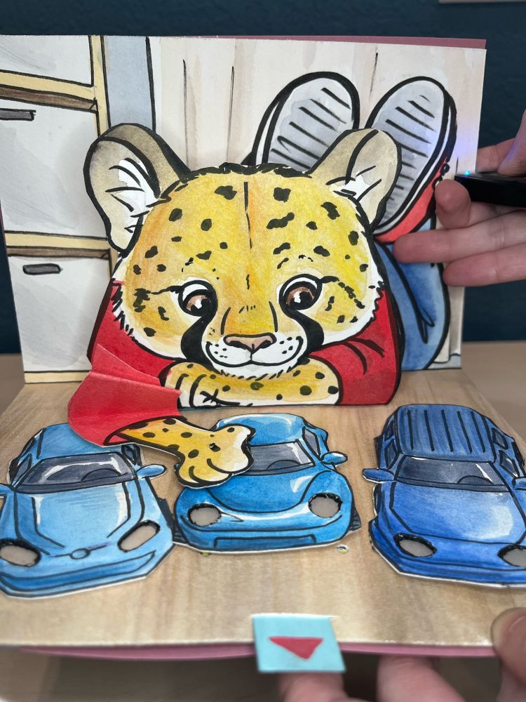 A pop up card with an anthropomorphized cheetah laying on the ground pushing toy cards into the correct order. When the cars move into place, their lights turn on.